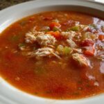Close-up of a bowl of rich, tomato-based maryland crab soup featuring visible chunks of flaked crab meat and diced vegetables.