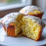 Close-up of a moist lemon poppy seed muffin cut in half, showing the texture and poppy seeds, topped with lemon glaze.