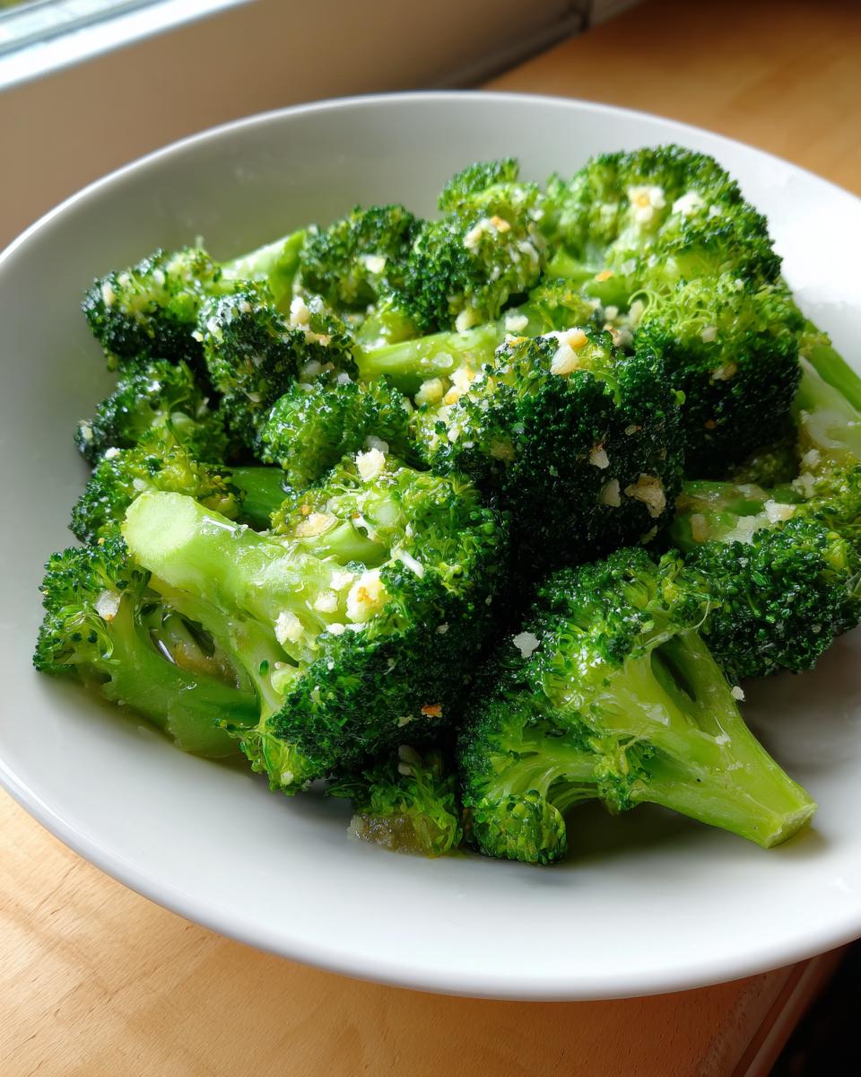 A close-up of vibrant, perfectly cooked steamed broccoli florets topped with minced garlic or seasoning in a white bowl.