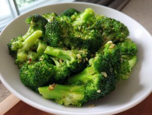 Close-up of bright green steamed broccoli florets seasoned with garlic and red pepper flakes in a white bowl.