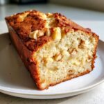 Close-up of a thick slice of hawaiian banana bread showing moist crumb, chunks of banana, and visible nuts.