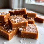 Close-up of soft chewy caramels cut into squares and sprinkled generously with flaky sea salt.