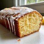 Close-up of a moist sourdough discard lemon loaf, sliced to show the crumb, topped with dripping white lemon glaze.