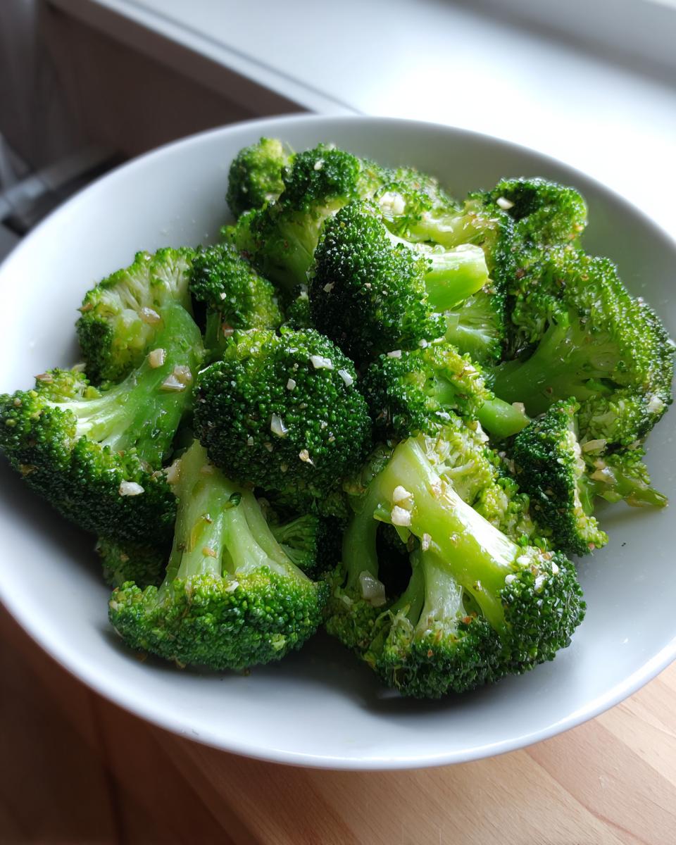 A white bowl filled with bright green steamed broccoli florets seasoned with minced garlic.