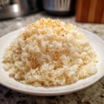 A mound of fluffy white texas roadhouse seasoned rice topped with visible spices on a white plate.