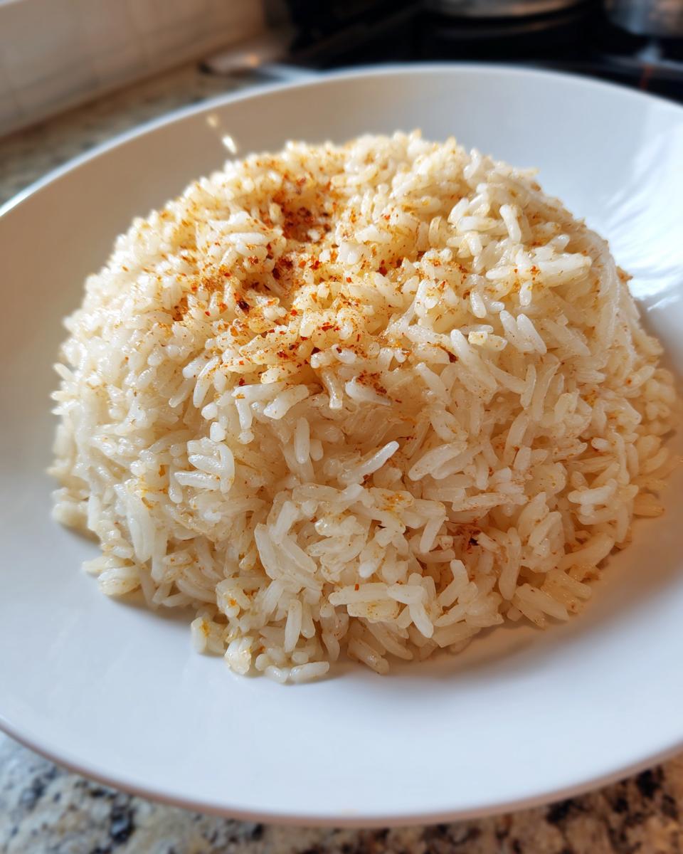 A mound of fluffy white rice, resembling texas roadhouse seasoned rice, topped with a light dusting of reddish-brown spices.